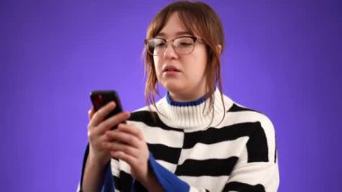 20 'li yaşlarda, mutlu gülümseyen genç bir kadının portresi cep telefonuyla konuşarak mor arka plan stüdyosunda izole edilmiş hoş sohbetler yaparak..