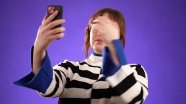 Mutlu gülümseyen 20 'li yaşlardaki genç bir kadının portresi mor arka plan stüdyosunda izole edilmiş hoş sohbetler yapan cep telefonuyla selfie çekiyor..