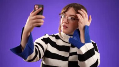 Mutlu gülümseyen 20 'li yaşlardaki genç bir kadının portresi mor arka plan stüdyosunda izole edilmiş hoş sohbetler yapan cep telefonuyla selfie çekiyor..