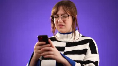 Sinirli, sosyal medya ya da haberler için stüdyodaki genç bayanla mesajlaşmanın portresi. Çevrimiçi dolandırıcılık, spam ve hayal kırıklığına uğramış mor arka plandaki kadın..