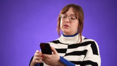 Mutlu gülümseyen 20 'li yaşlardaki genç bir kadının portresi. Mor arka plan stüdyosunda izole edilmiş akıllı telefon bilgisayarından fotokopi alanı ile online alışveriş yapıyor.