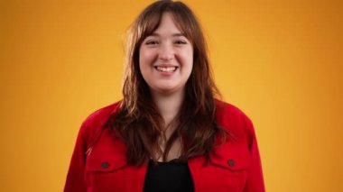 Kahverengi saçlı, kırmızı ceketli, mutlu, genç bir kadın. Sarı arka planda izole edilmiş, fotokopi alanı ağır çekimde.