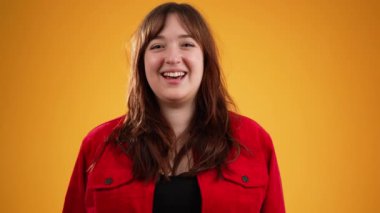 Kahverengi saçlı, kırmızı ceketli, mutlu, genç bir kadın. Sarı arka planda izole edilmiş, fotokopi alanı ağır çekimde.