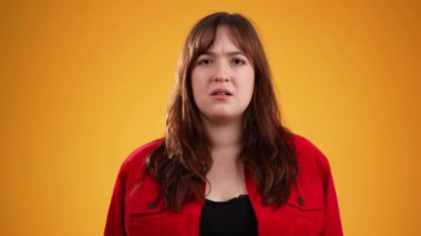 Kahverengi saçlı, mutsuz, kırmızı ceketli genç bir kadın. Kafası HAYIR 'ı sallıyor. Sarı arka planda izole edilmiş ve fotokopi alanı ağır çekimde.