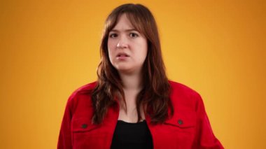 Kahverengi saçlı, kırmızı ceketli, mutsuz genç bir kadın başını sallıyor. Durma hareketinde hayır diyor. Sarı arka planda izole edilmiş ve fotokopi alanı yavaş çekimde.