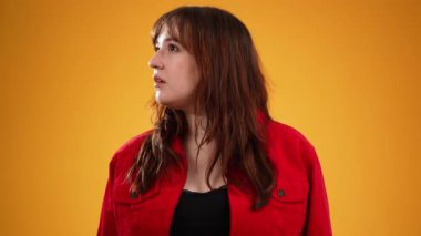 Genç, mutlu, gülümseyen güzel kadın iki tarafa da bakıyor ve sonra kameraya gülümsüyor. Kahverengi saçlı, sarı arka planda izole edilmiş kırmızı ceketli ve fotokopi çeken bir kadın.