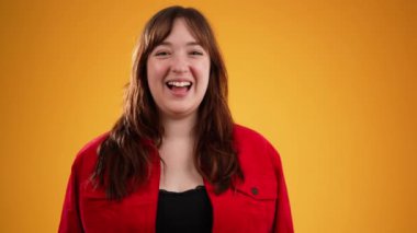 20 'li yaşlarda, kırmızı ceketli genç bir kadın sarı arka plandaki stüdyoda izole edilmiş birini görünce el sallıyor. İnsanlar yaşam tarzı kavramını resmediyor