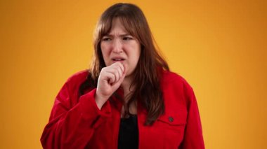 20 'li yaşlarda, öksürük ve boğaz ağrısı çeken genç bir kadının portresi. Stüdyoda sarı arka planda, fotokopi odasında yavaş çekimde izole edilmiş.