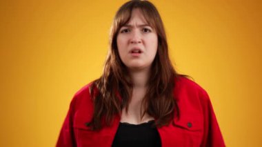 Sinirli, mutsuz, esmer, genç, kırmızı ceketli, el kol hareketleri yapan bir kadın. Stüdyoda parmağını kulaklarına sokmadığını söylüyor. İnsanlar samimi duygular, yaşam tarzı konsepti.