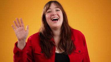 20 'li yaşlarda, kırmızı ceketli genç bir kadın sarı arka plandaki stüdyoda izole edilmiş birini görünce el sallıyor. İnsanlar yaşam tarzı kavramını resmediyor