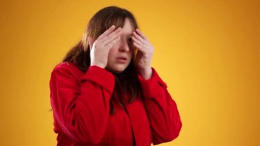 20 'li yaşlardaki korkmuş esmer kadın sarı arka plan stüdyosunda yalnız poz veriyor. İnsanların yaşam tarzı konsepti. Ağız kaplayan gözler ve saklanan eller.