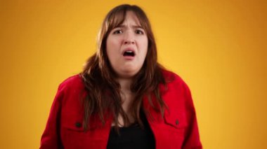 20 'li yaşlardaki korkmuş esmer kadın sarı arka plan stüdyosunda yalnız poz veriyor. İnsanların yaşam tarzı konsepti. Ağız kaplayan gözler ve saklanan eller.