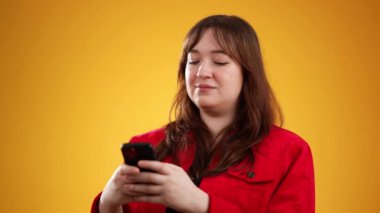 20 'li yaşlarda mutlu gülümseyen genç bir kadının portresi akıllı telefon bilgisayarından alışveriş yapıyor sarı arka plandaki stüdyoda fotokopi alanı ile izole edilmiş.