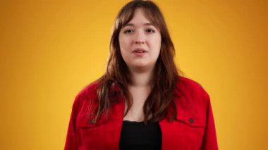 20 'li yaşlardaki güzel düşünceli genç bir kadının portresi, kameraya bakıyor, akıllara durgunluk veren jestler yapıyor, sarı arka planda fotokopi alanı ile fikirlerin patlamasını gösteriyor..