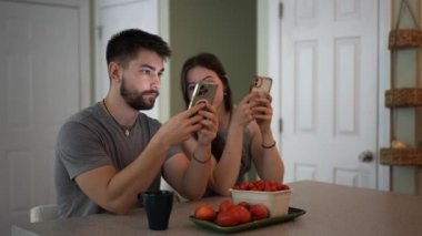 Kamera, mutfak tezgahında oturan genç bir çifti görüntülemek için geri çekiliyor. Telefonla mesajlaşıyorlar, evde çalışıyorlar..