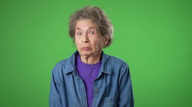 Mutlu yaşlı yaşlı kadın portresi, buruşuk derili, gri saçlı, omuzlarını silkeleyen ve yeşil ekranda izole edilmiş bir şekilde el kol hareketi yapan yaşlı kadın..