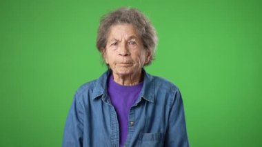 Kızgın, sinirli, yaşlı ve yaşlı bir kadının portresi. Cildi kırış kırış, saçları kırış kırış ve yeşil perde arkasında..