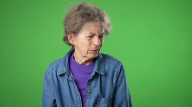 Sağlık sorunu olan yaşlı bir kadının portresi. Omuz ağrısı, kırışık cilt ve yeşil perde arkasında gri saçlar..