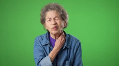 Sağlık sorunu olan yaşlı bir kadının portresi. Boyun ağrısı, buruşuk cilt ve yeşil perde arkasında gri saçlar..