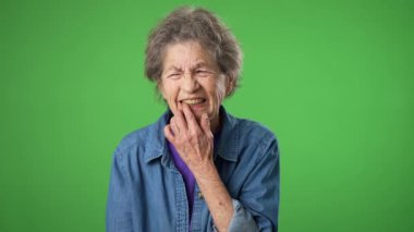 Diş ağrısı sorunu olan yaşlı bir kadının portresi stüdyodaki yeşil ekranda izole edilmiş.