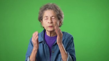Hasta baş ağrısı migreni portresi bitkin yaşlı bir kadının yeşil ekran arka plan stüdyosunda yalnız poz verişi. Ellerini baş masajına koy