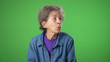Beyaz tenli, yaşlı, yaşlı, buruşuk tenli, gri saçlı bir kadının portresi yeşil ekran arka plan stüdyosunda izole edilmiş bir sırrı dinlemek için kulaklarını tıkıyor.