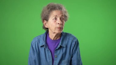 Bir sır vermek için kıt kanaat ağza vermek. Yaşlı yaşlı bir kadının portresi. Kırışık derili, gri saçlı, yeşil ekran arka plan stüdyosunda izole edilmiş.