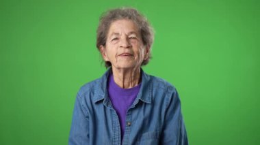 Buruşuk derili ve gri saçlı yaşlı bir kadının portresi yeşil ekran arka planında izole edilmiş el hareketleriyle işaret veriyor.