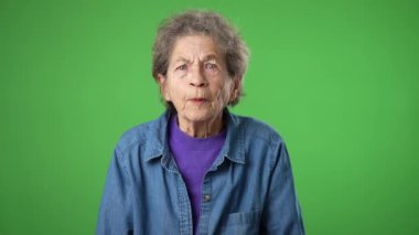 Hoşnutsuz, sinirli, sinirli, yaşlı, yaşlı, buruşuk derili, gri saçlı, gözleri kapalı, kulakları kapalı yaşlı kadın yeşil ekran arka plan stüdyo resminde izole edilmiş çığlıkları dinlemek istemiyor.
