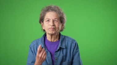 Mutlu yaşlı yaşlı kadın portresi, buruşuk derili, gri saçlı, gülümseyen, huzur veren ve zafer işareti yapan yeşil ekranlı arka planda elleri olan yaşlı kadın..