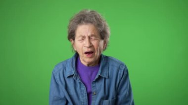 Yorgun, uykulu, yaşlı yaşlı bir kadının portresi. Pörsümüş derisi ve gri saçları, yeşil ekran arkasında izole edilmiş..