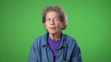 Yorgun, uykulu yaşlı bir kadının portresi dua ederken el ele tutuşup dilek tutarak yeşil ekran arka plan stüdyosunda parmaklarını çapraz tut..