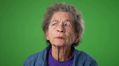 Sinirli ümitsizliğin yavaş çekimde portresi, yeşil ekranda izole edilmiş kırışık derili ve gri saçlı yaşlı bir kadının üzgün portresi..