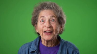 Yakın çekim, heyecanlı, yaşlı, gülümseyen yaşlı bir kadının portresi. Kırışık ciltli, yeşil ekran arka planında gri saçlı yaşlı bir kadın..