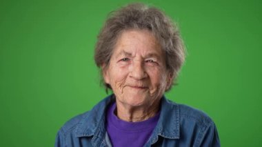 Kapalı çekim yavaş çekim portresi. Dişsiz, mutlu, yaşlı, gülümseyen, yaşlı, buruşuk derili ve yeşil ekran arka planında gri saçlı bir kadın..