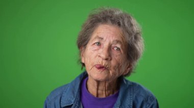 Düşünceli, dişsiz, dişsiz, yeşil ekranda dili çıkmış yaşlı bir kadının yavaş çekim portresi..