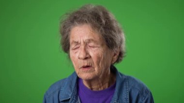 Depresyondaki yaşlı, dişsiz, yaşlı, 80 'li yaşlarda, migren ağrısı olan, yeşil ekran arka plan stüdyosunda izole edilmiş yaşlı bir kadın. İnsanların yaşam tarzı kavramına yakın olmak. Yüzünü dön.