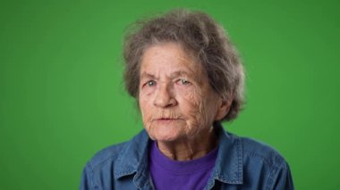 Dişsiz, sinirli, sinirli, sinirli, yaşlı ve yaşlı bir kadının portresi. Kırışık derili, yeşil ekran arka planında gri saçlı..