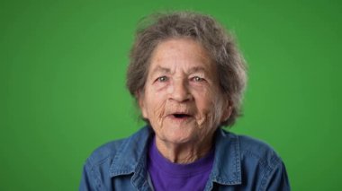Dişsiz, yaşlı, buruşuk derili ve gri saçlı yaşlı bir kadının yeşil ekranda izole edilmiş başarılı kazananı ile mutlu olan yavaş çekimde portresi. Duygular konsepti
