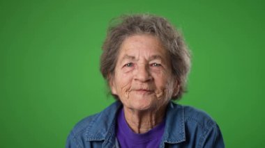 Yavaş çekimde gülümseyen, dişsiz, yaşlı, buruşuk derili ve gri saçlı yaşlı bir kadının stüdyodaki yeşil ekran arka planında çekilmiş portresi. Duygular konsepti