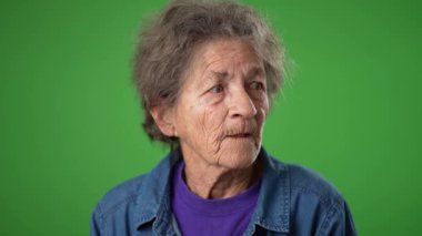 Kapalı çekimde, yaşlı, dişsiz yaşlı bir kadının portresi. Kırışık derili, kır saçlı, yeşil ekran arka plan stüdyosunda izole edilmiş bir sırrı anlatmak için ağızdan ağıza konulmuş.