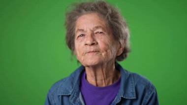 Elini dişsiz ağıza koy ve bir sır ver. Yaşlı yaşlı, buruşuk derili, yeşil ekran arka plan stüdyosunda izole edilmiş gri saçlı bir kadının komik, yavaş çekimde yakın plan portresi.