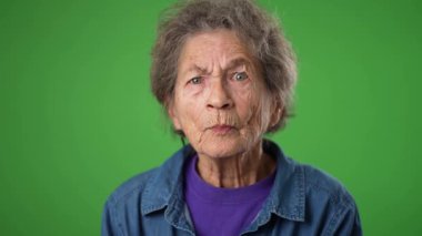 Yavaş çekimde gülümseyen, yaşlı, buruşuk derili, gri saçlı yaşlı bir kadının komik portresi. Bana, yeşil ekranda HAYIR yazan kişinin kim olduğunu sor.