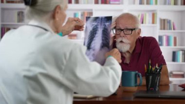 Kadın doktor yaşlı bir adama röntgen filmi gösteriyor, yaşlı bir hastaya, profesyonel sağlık sigortası sağlıyor..