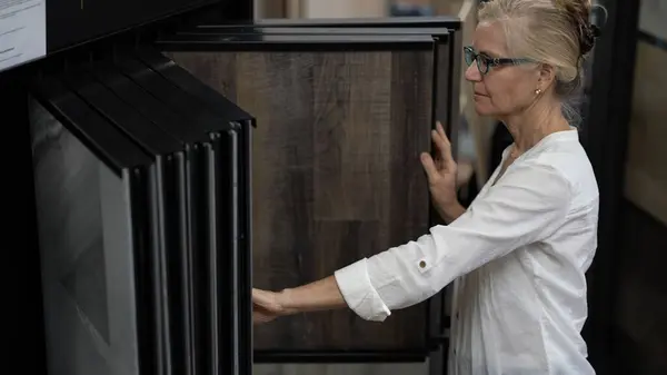 stock image Happy mature woman touching luxury vinyl tile plank samples in a floor store for a home remodeling, redecorating, or renovation project.