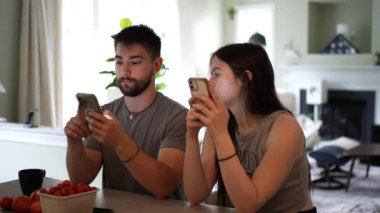 Charlottesville, VA, ABD - 07 24 2024: Kamera ev mutfağındaki telefonları kullanan hippi genç çiftin etrafında hareket ediyor.