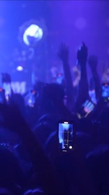 Bir konser ya da festival partisinde dans eden tanınmayan hayranların dikey videosu. Konser kalabalığının siluetleri yanıp sönen sahne ışıkları önünde
