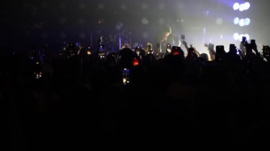 Bir konser ya da festival partisinde dans eden tanınmayan hayranların dikey videosu. Konser kalabalığının siluetleri yanıp sönen sahne ışıkları önünde