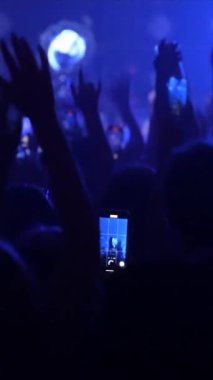 Bir konser ya da festival partisinde dans eden tanınmayan hayranların dikey videosu. Konser kalabalığının siluetleri yanıp sönen sahne ışıkları önünde