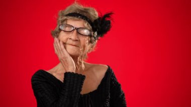 Gülümseyen yaşlı bir kadının komik portresi. 80 'li yaşlarda harika anılar düşlüyor, düşünüyor, kırmızı stüdyo arka planında izole edilmiş ve fotokopi alanı olan.